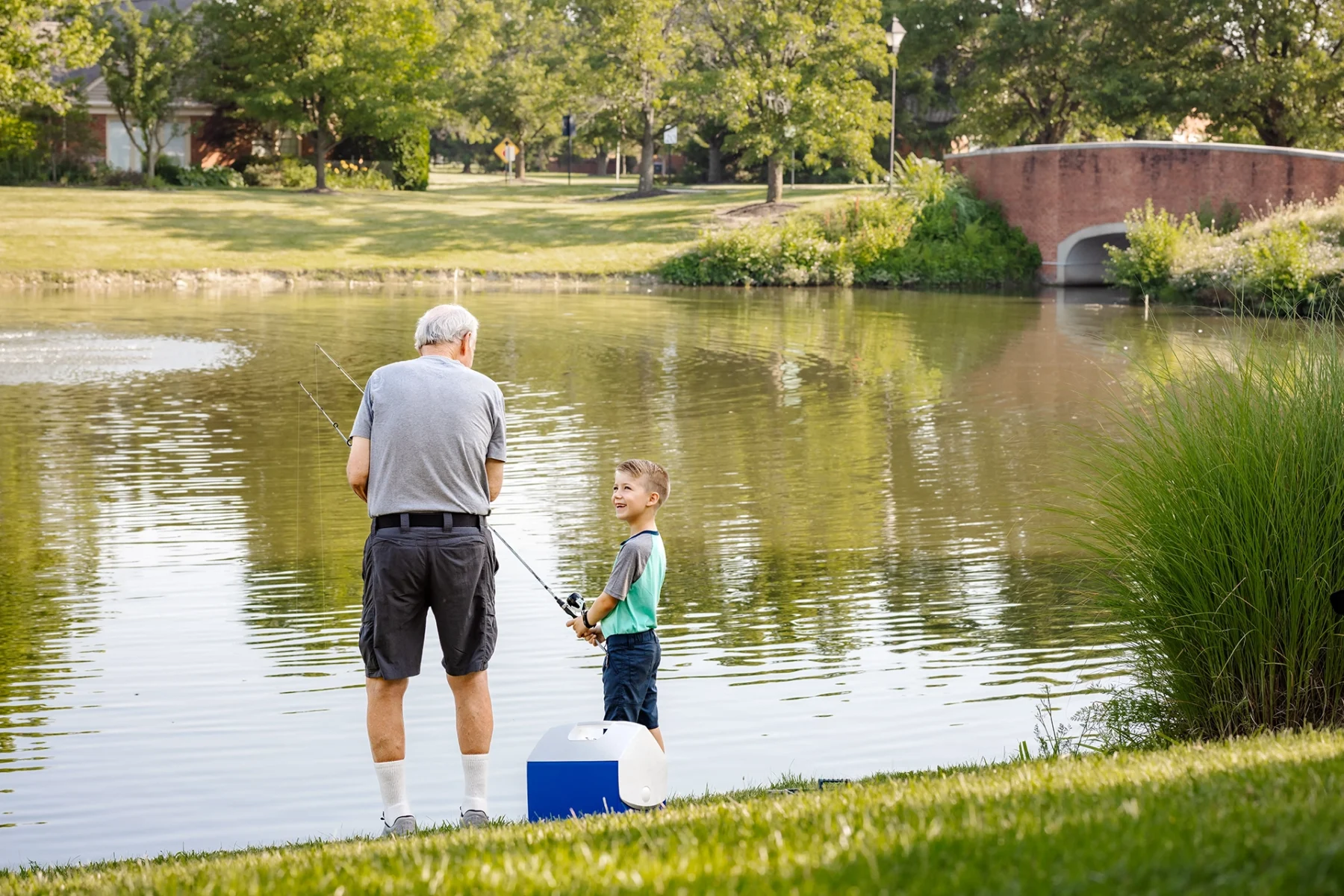 Berkeley Square senior living resident fishing in the community pond with his grandson