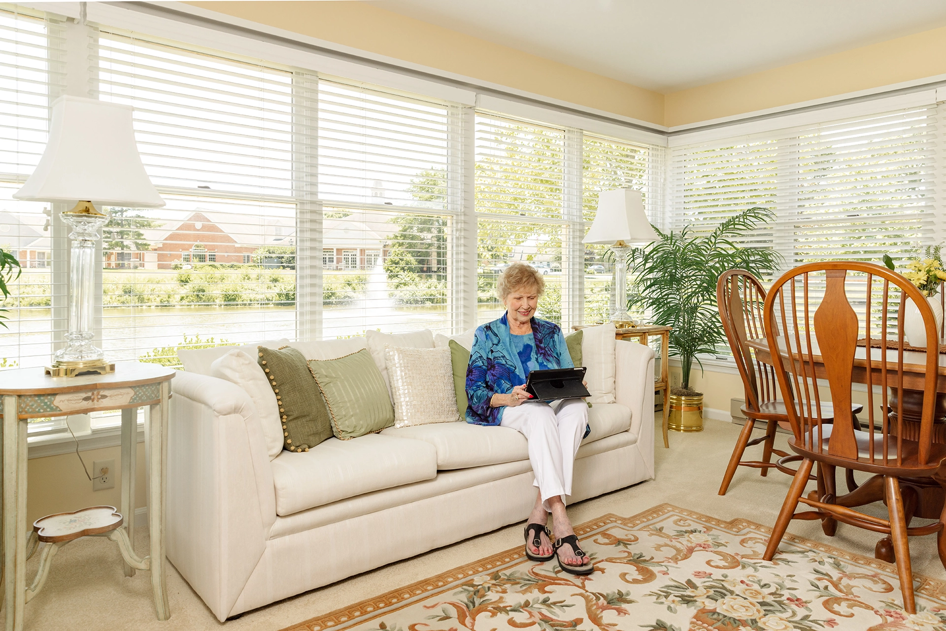 Berkeley Square senior living resident sitting on the couch with a tablet in her sunroom