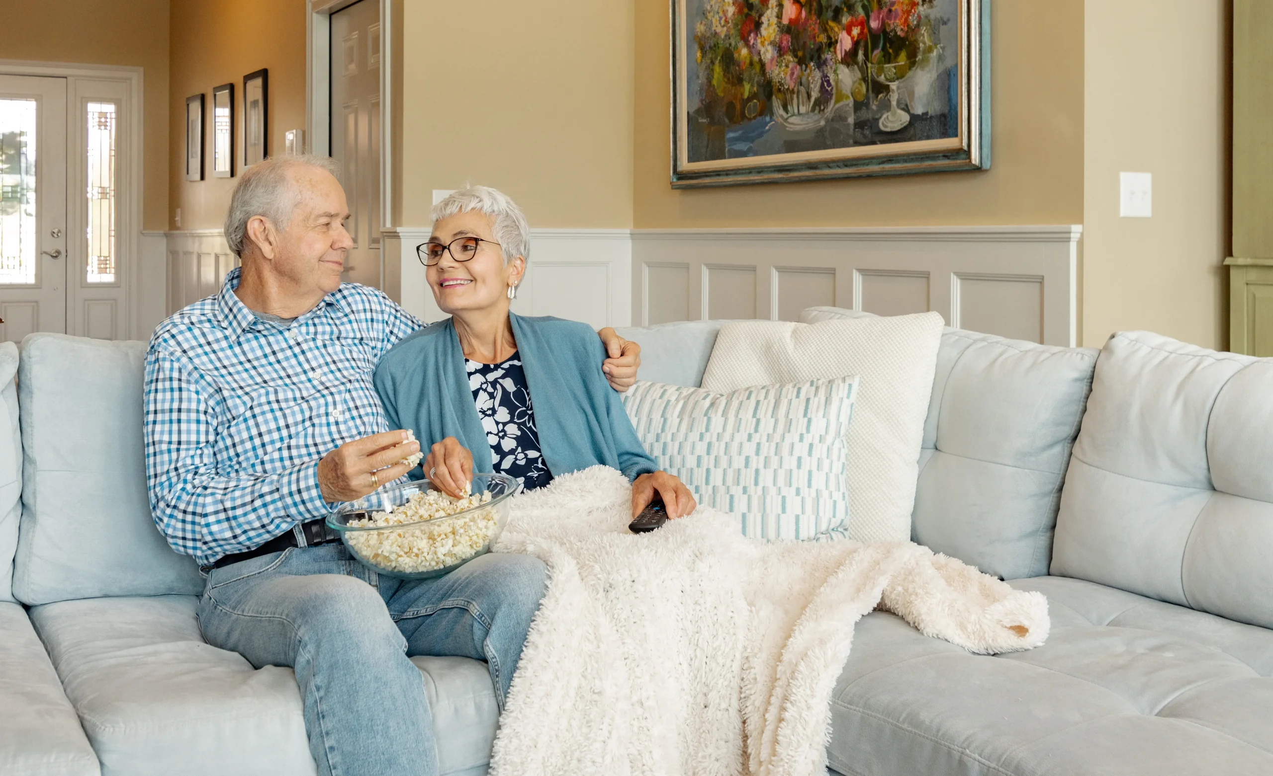 Senior living couple snuggle on the couch together eating popcorn inside an independent living home