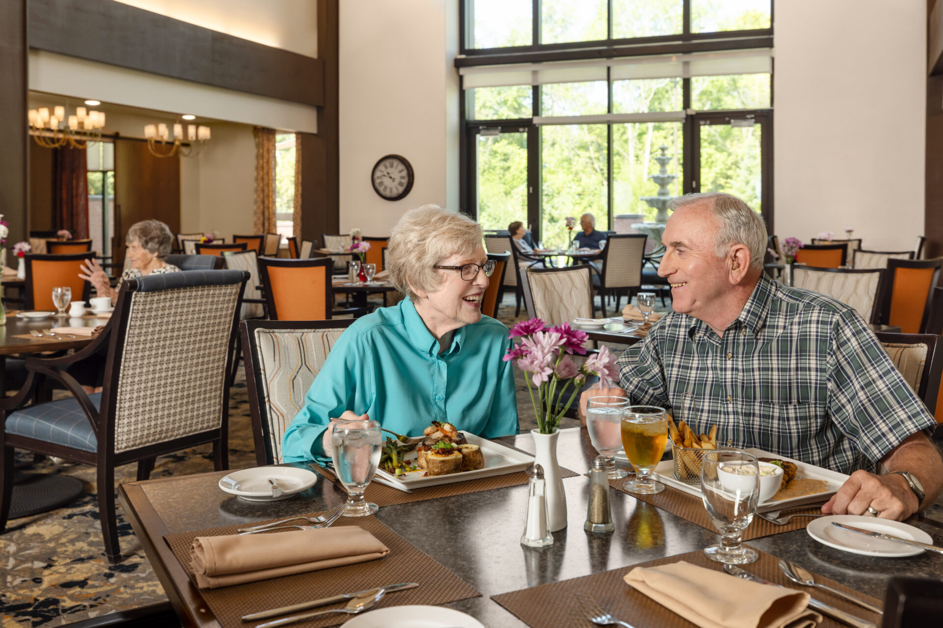 Residents enjoying a meal together in the elegant dining room, featuring soaring ceilings and comfortable seating at The Patterson