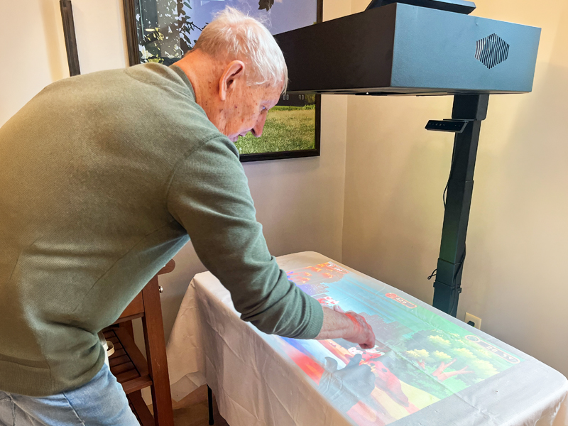Senior man leans over the Lucynt Table, touching a colorful projected nature scene during a TouchPoint Sensory activity