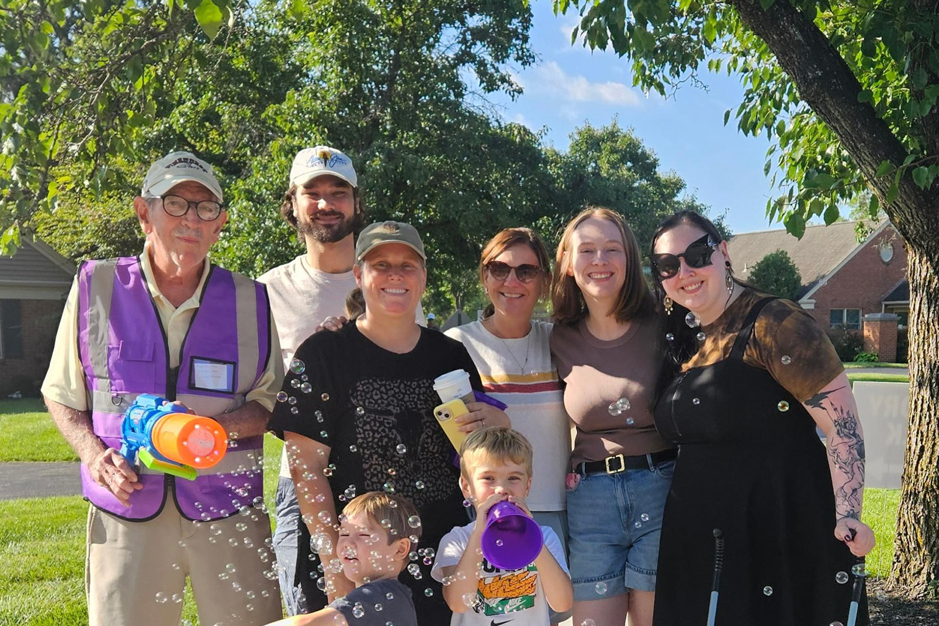 A multigenerational group of walkers laughs together outdoors at Berkeley Square's Memory Care Walk, surrounded by bubbles